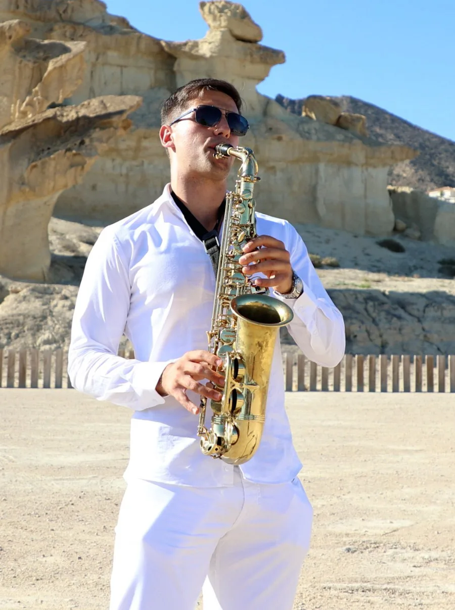 Saxofonista con traje blanco tocando ante unas formaciones de arenisca.