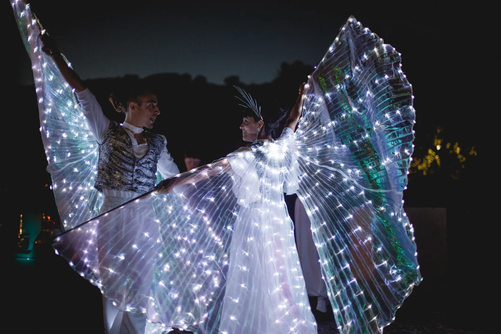 Dos artistas con alas LED desplegadas en una actuación nocturna