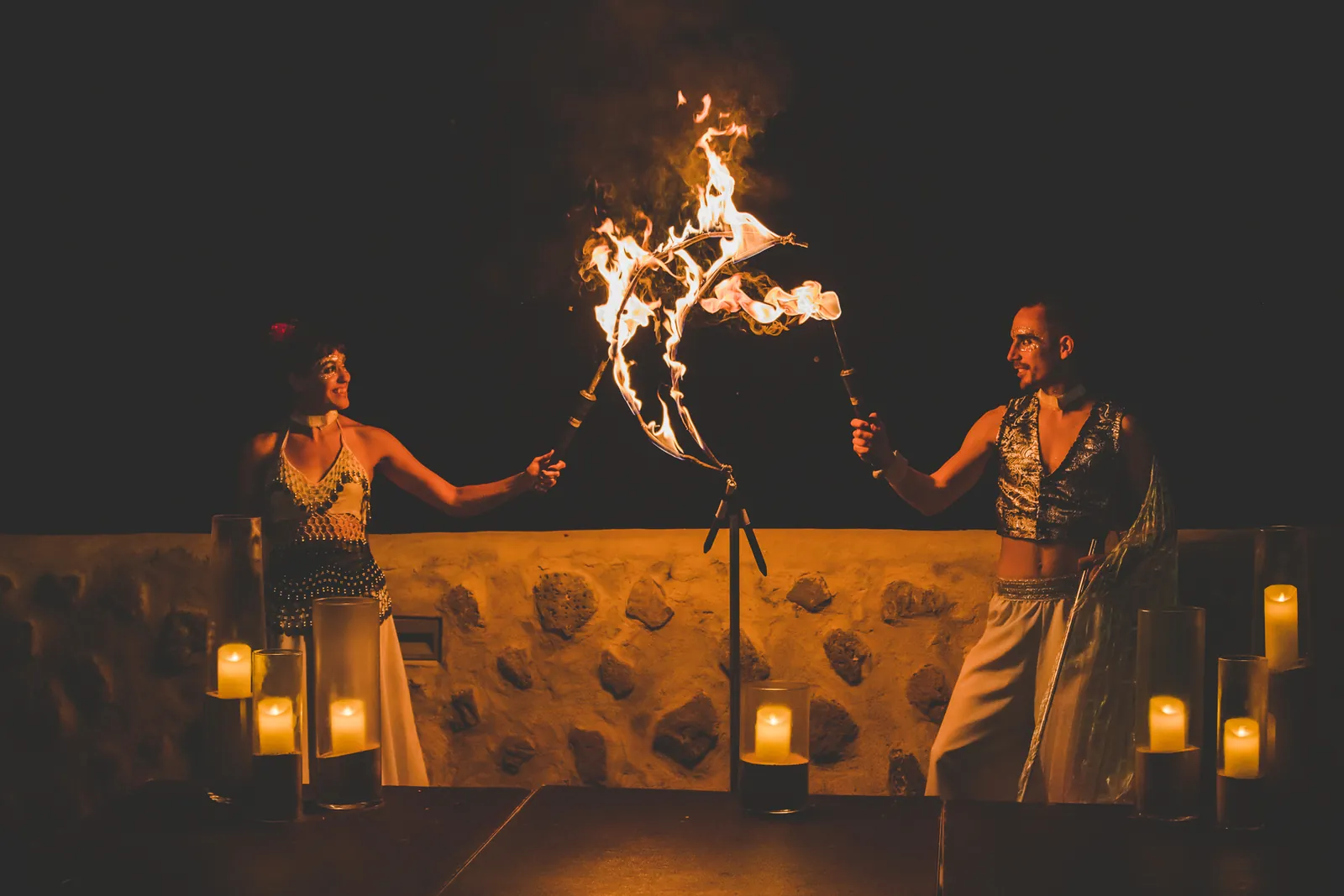 Dos artistas haciendo girar fuego ante una terraza iluminada con velas