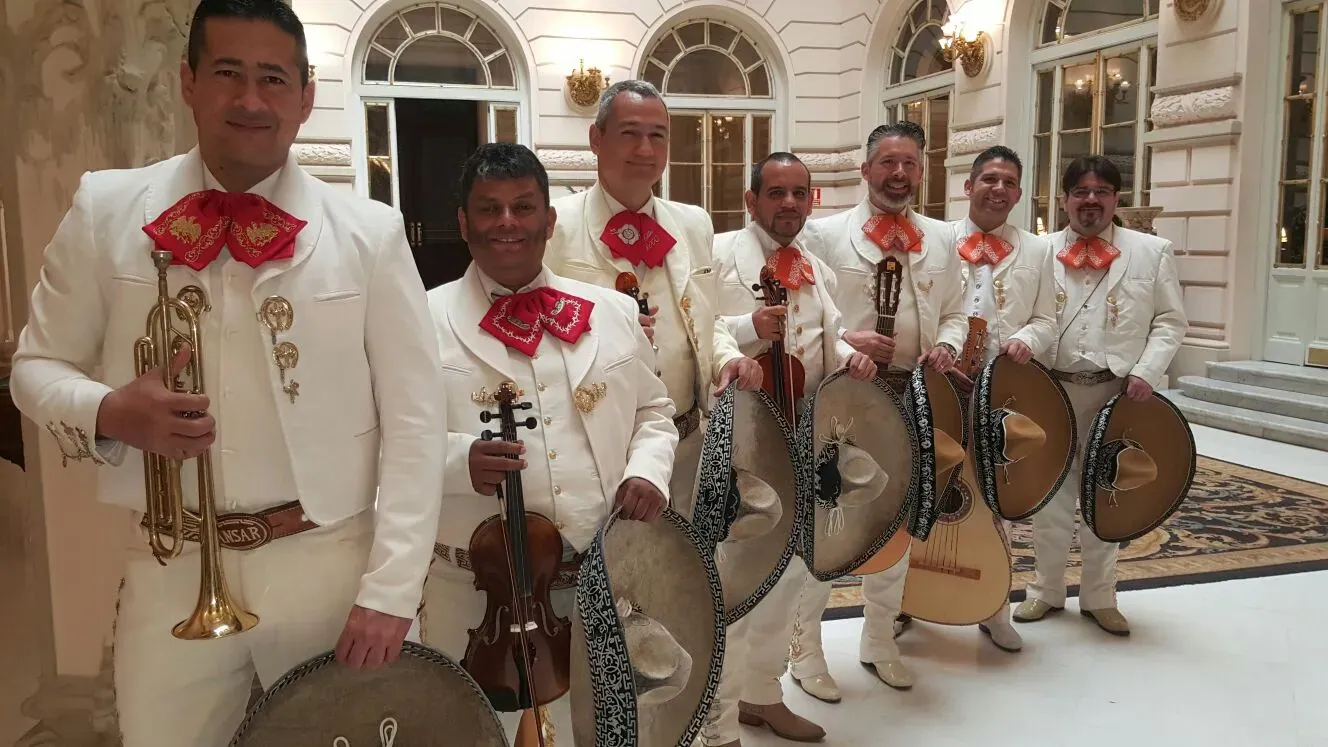 Mariachis con trajes blancos y corbatín rojo posando en un salón señorial