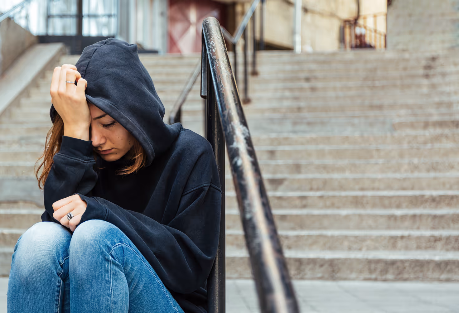 Teen in a hoodie sitting alone on steps looking upset
