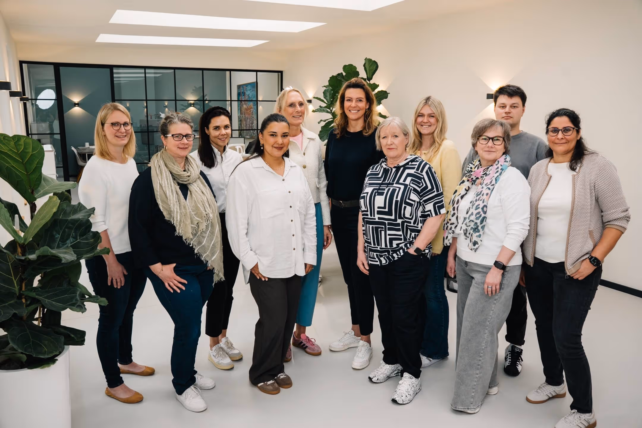 Gruppenfoto von elf Personen, die freundlich in einem modernen, hellen Büro stehen.