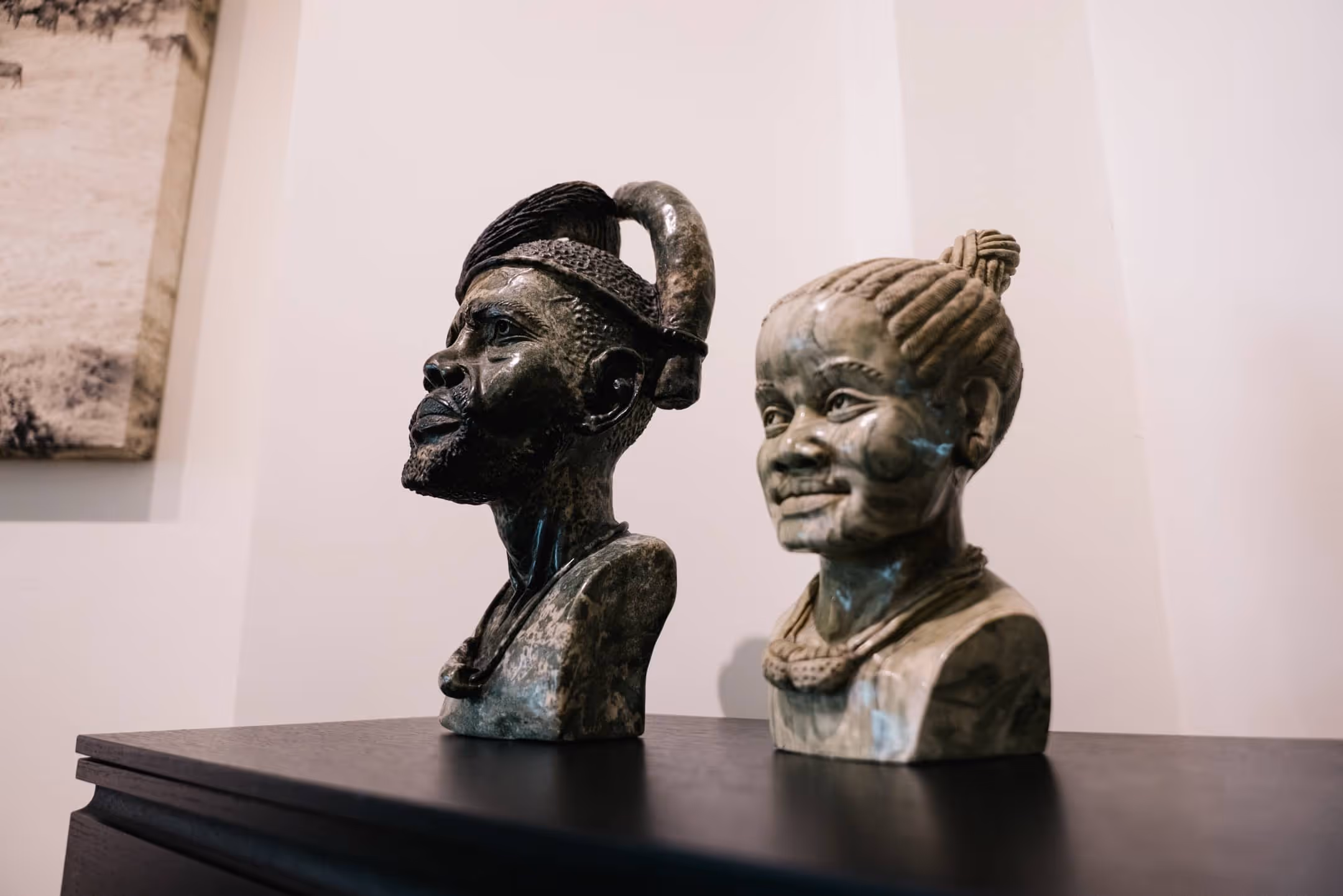 Zwei detailreiche afrikanische Büsten-Skulpturen aus Stein, eine männlich mit Kopfbedeckung und eine weiblich mit geflochtenem Haar.