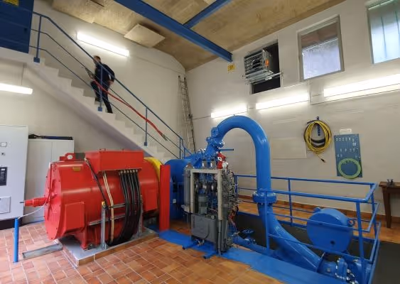Industrial room with large red and blue machinery and a person walking up stairs in the background.
