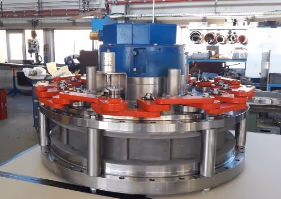 Industrial machine component with metallic circular base and red mechanical arms in a workshop.