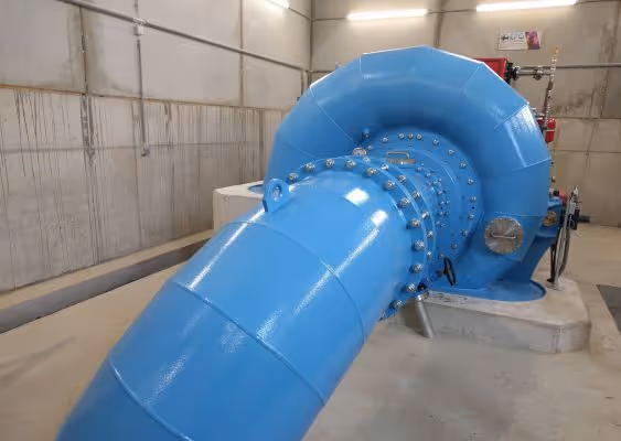 Large blue industrial pipe and valve system inside a concrete-walled facility.