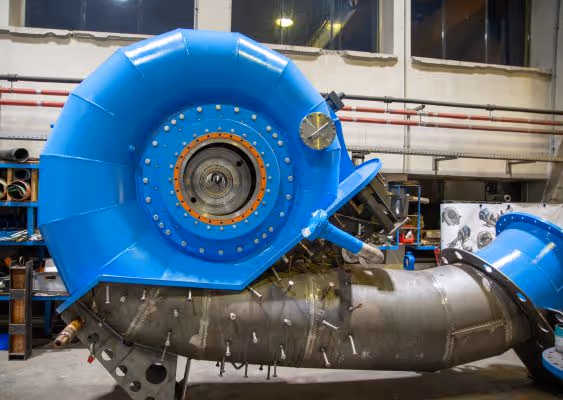 Large industrial turbine housing painted blue mounted on a metal base inside a workshop.