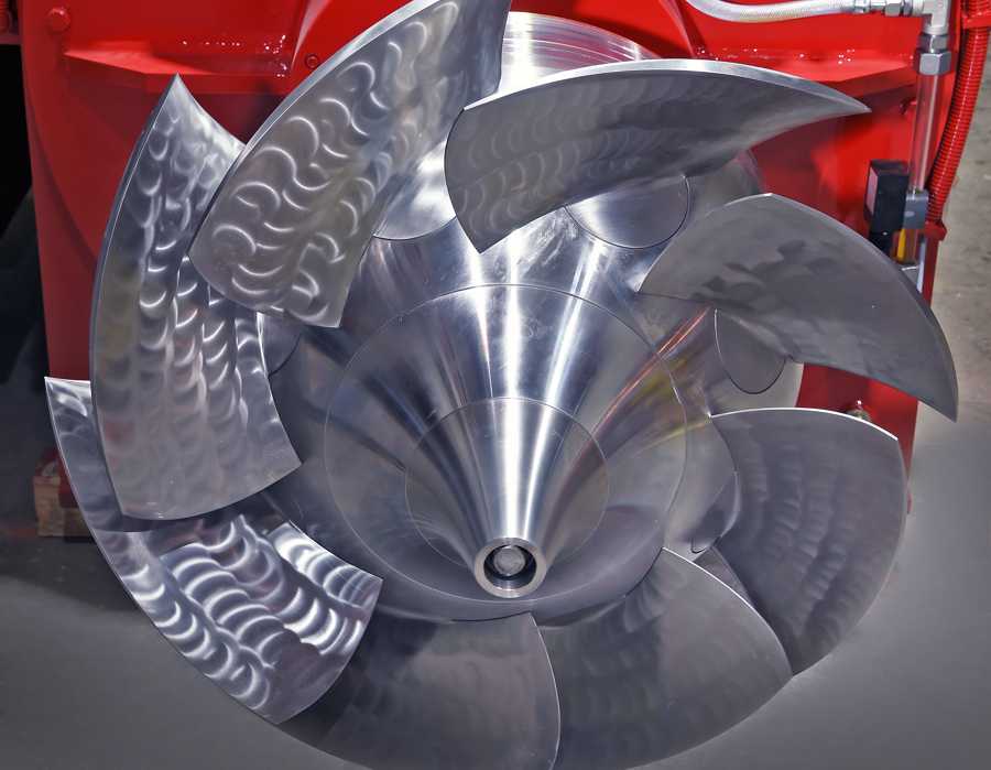 Close-up of a large shiny metallic turbine impeller with curved blades inside a red casing.