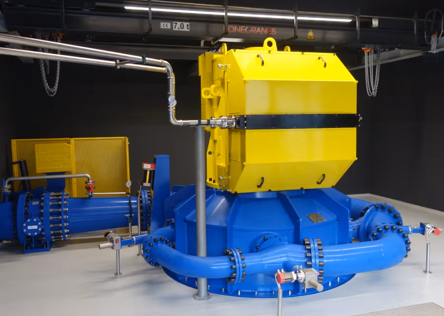 Large industrial Pelton turbine with bright yellow and blue components in a clean, dimly lit room.