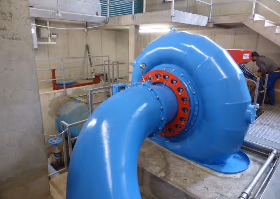 Large blue industrial pipe connected to machinery inside a concrete facility with a worker in the background.