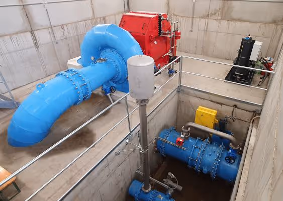 Industrial setting with large blue pipes, a red machine, and metal railings inside a concrete facility.