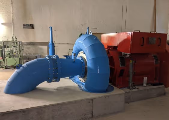 Large blue industrial pipe connected to a red machine inside a concrete-floored facility.