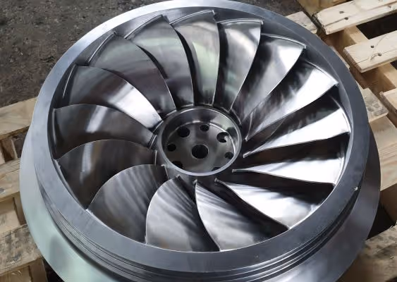 Close-up of a metallic turbine impeller with curved blades resting on wooden pallets.
