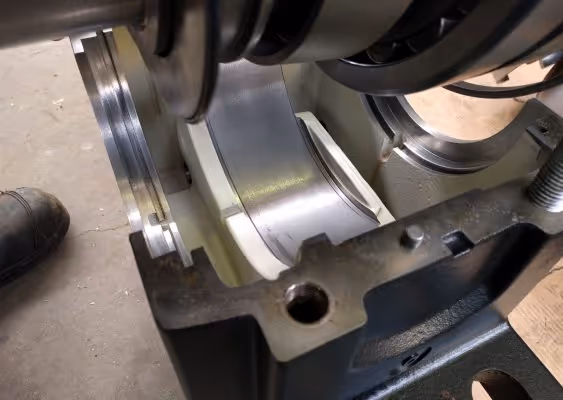 Close-up of a metallic bearing shell seated in a black engine block with part of a boot visible on the left side.