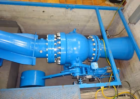 Blue industrial pipe valve assembly installed in a concrete enclosure with connected yellow and green cables.