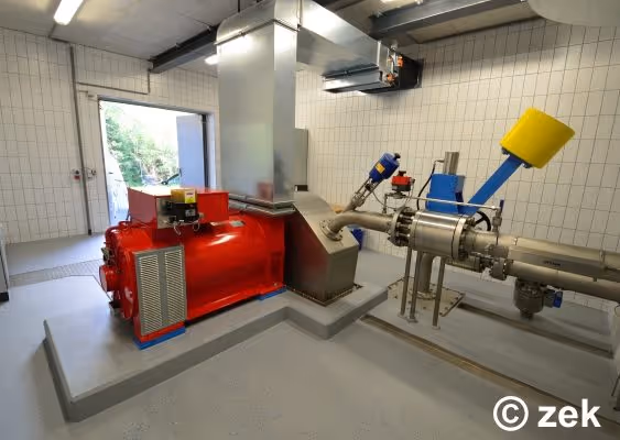 Industrial room with a large red machine connected to metallic pipes and ventilation ducts on tiled walls.