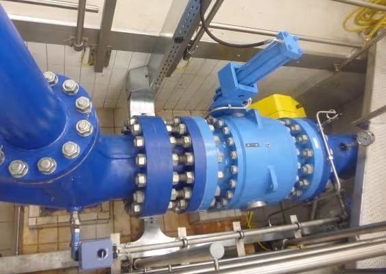 Blue industrial pipeline with large bolted flanges and a valve or actuator in a mechanical room.