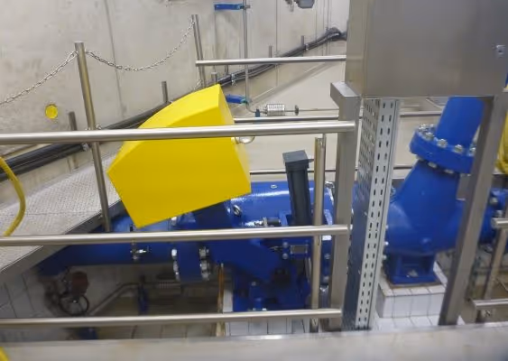 Industrial blue machinery with a yellow protective cover inside a metal railing enclosure in a facility.