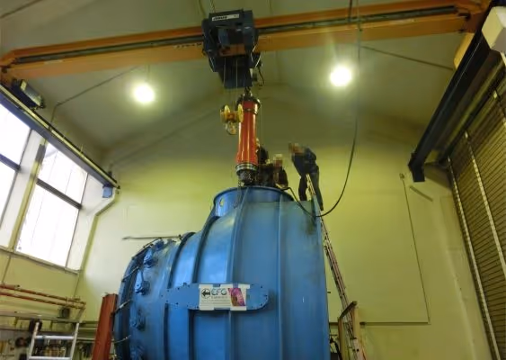 Two workers performing maintenance on large blue industrial machinery inside a factory.