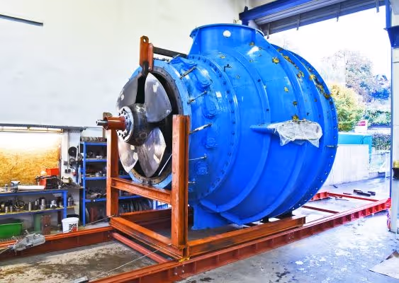 Large blue industrial turbine or generator housed in a wooden frame inside a workshop.