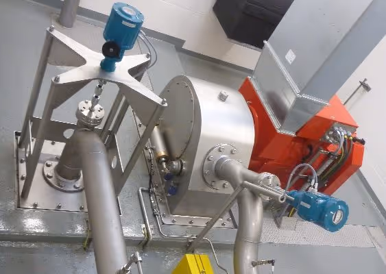 Industrial machinery featuring stainless steel pipes, sensors, and a red and silver metal housing unit in a clean facility.