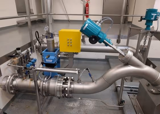 Industrial metal piping system with blue and yellow control units inside a facility.