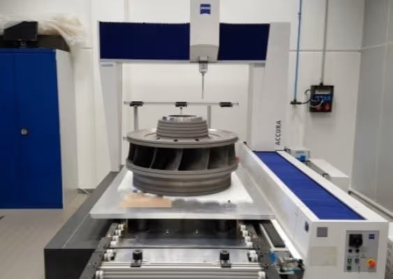 Industrial coordinate measuring machine inspecting a large metallic turbine component in a clean, white room.