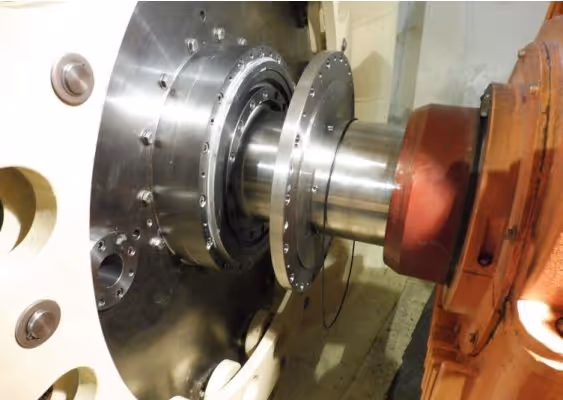 Close-up of a large metallic industrial machine shaft connected to an orange mechanical component.