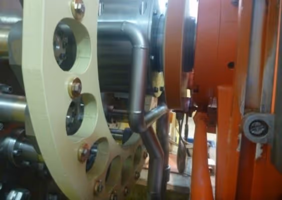 Close-up of a complex industrial machine with metal pipes, bolts, and orange components.