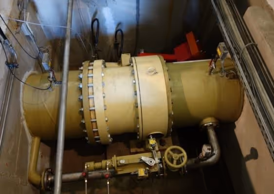 Large industrial yellow metal pipe with valves and fittings in a dimly lit utility or mechanical room.