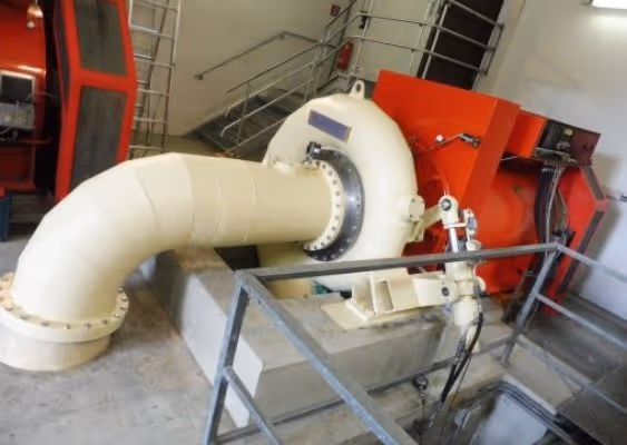 Industrial turbine with large white pipe connected to a red machinery unit inside a facility.