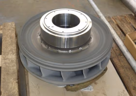 Industrial metal impeller or turbine component resting on a wooden pallet in a workshop.