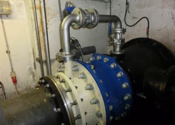 Industrial water pump system with large flanged piping and blue pump housing inside a utility room.