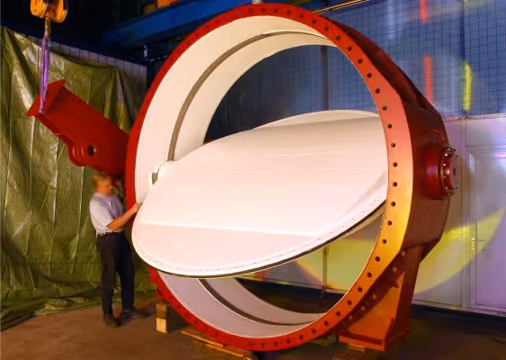 Large industrial red and white butterfly valve with a person standing next to it for scale in an indoor workshop.