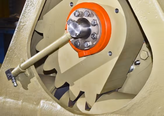 Close-up of a large industrial gear mechanism with multiple beige cogwheels and a central orange circular mount with bolts and a metal rod attached.