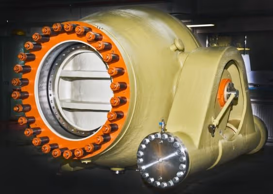 Large industrial machine component with a circular flange featuring orange bolts and a metallic circular end with smaller bolts.