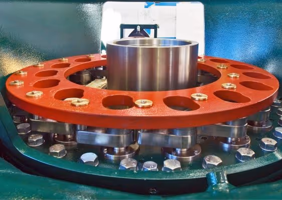 Close-up of industrial metal machinery part featuring a red circular plate with multiple holes and bolts surrounding a central cylindrical component.