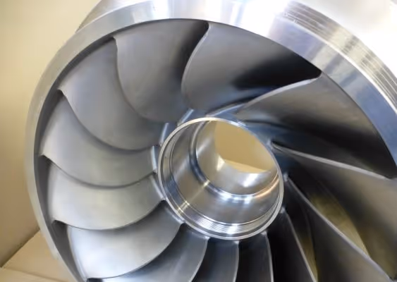 Close-up of a shiny metallic turbine or compressor impeller with curved blades.