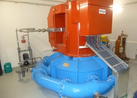Large industrial machine with blue curved pipes and an orange upper section inside a clean facility.