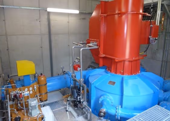 Industrial machinery with large blue and red components connected by metal pipes inside a facility.
