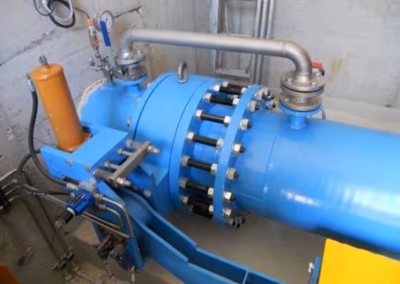Blue industrial pipeline with metal flange connections and attached valves in a concrete room.