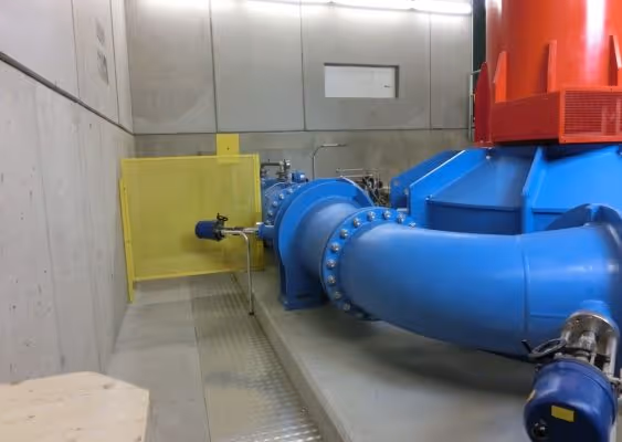 Large blue industrial pipe connected to a red machine inside a concrete-walled facility.