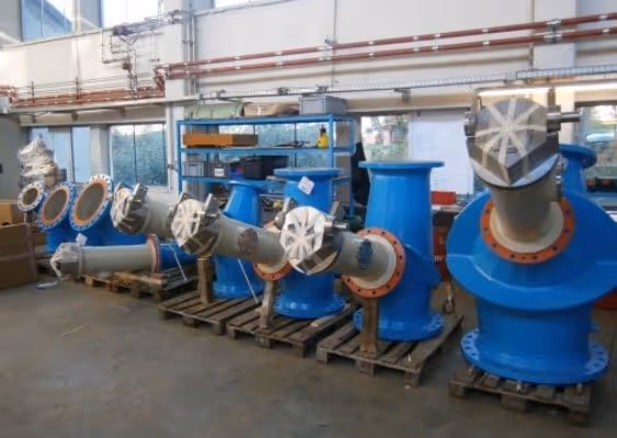 Industrial blue metal pipes and fittings lined up on wooden pallets inside a factory warehouse.