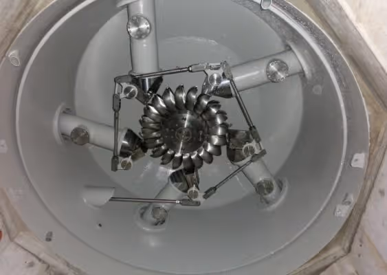 Top-down view of a metallic turbomachinery component with curved blades inside a circular enclosure.