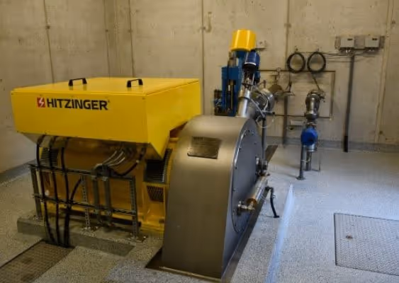 Industrial yellow Hitzinger generator set installed on a concrete floor in a utility room with metal pipes and gray walls.
