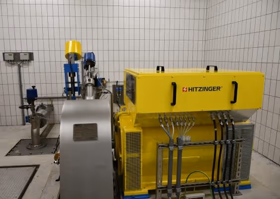 Industrial yellow Hitzinger machine with connected pipes and valves in a tiled room.