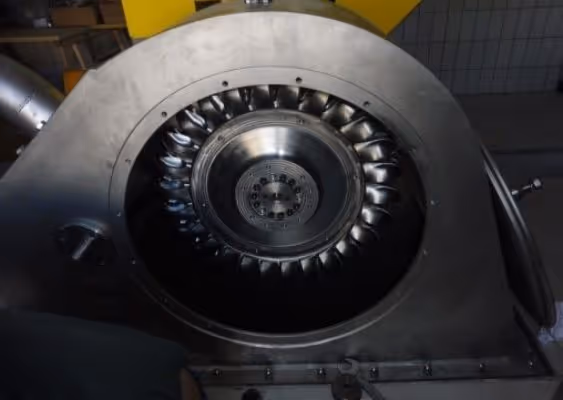 Close-up of a metallic industrial turbine or blower with curved blades inside a circular housing.