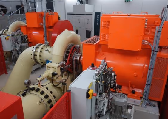 Industrial machinery with large beige pipes and bright orange equipment in a clean mechanical room.