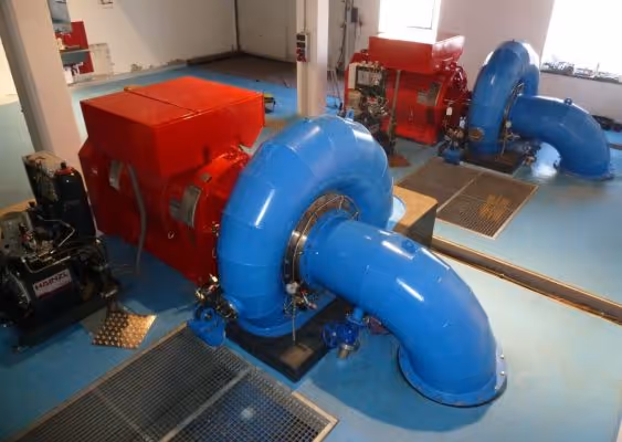 Interior view of a mechanical room featuring large blue industrial pipes connected to red machinery on a clean blue floor.