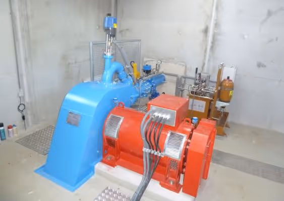 Industrial generator setup with a blue turbine connected to a red electric generator in a clean facility.